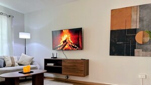 A modern living room with a flat-screen TV mounted on the wall, a wooden TV stand, a round coffee table, and a grey sofa. - Casa Luma is a calm, light-filled home designed for rest and simplicity. (Aguascalientes)
