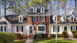 A row of townhouses with a central brick building, each with a front porch and a small front yard. - Floating Flamingo; Walk to Downtown Cary; Greenway; Close to Cary Park; Wake Med (Cary)