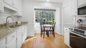 A kitchen with white cabinetry, a granite countertop, a dining table with chairs, and a large window with a view of greenery. - Floating Flamingo; Walk to Downtown Cary; Greenway; Close to Cary Park; Wake Med (Cary)