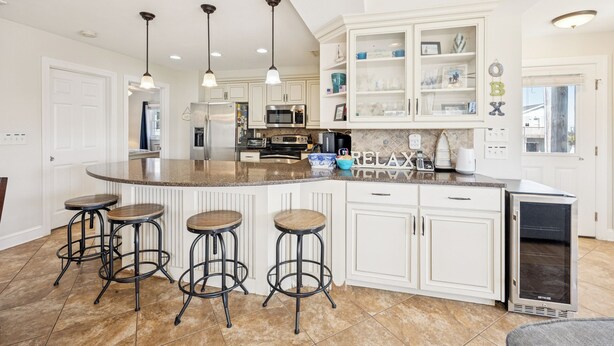 A spacious kitchen with a large island, bar stools, white cabinetry, and a built-in oven. - 8388 Family Island Retreat | Steps to Beach (Avon)