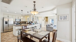 A modern kitchen with a central island, stainless steel appliances, pendant lighting, and a dining area with a bench and placemats. - 8388 Family Island Retreat | Steps to Beach (Avon)
