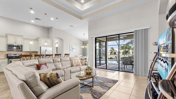 A spacious living area with a large beige sectional sofa, a glass coffee table, and a view of the outdoor patio. - Canalfront Island Escape with Pool, Lanai & Dock - Antigua Villa - Roelens (Cape Coral)