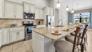 A kitchen with granite countertops, stainless steel appliances, and a large island with bar stools. - Canalfront Island Escape with Pool, Lanai & Dock - Antigua Villa - Roelens (Cape Coral)