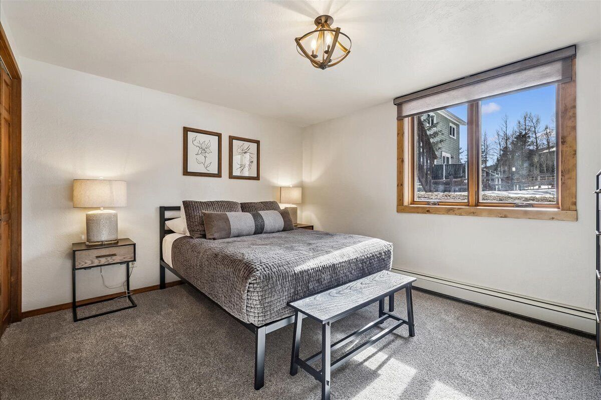 A bedroom with a bed, bedside lamps, a bench, and a window with a view of trees.