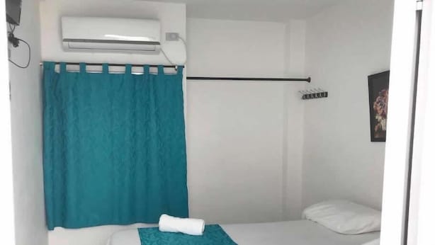 A small, single-bed room with a white bed, a teal curtain, a white pillow, and a white towel on the bed. - HOTEL URUMITA MAGICA (Valledupar)