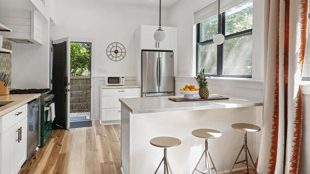 A modern kitchen with a central island, bar stools, a microwave, and a refrigerator. - Designer Inman Park | Beltline Steps (Atlanta)