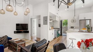 A modern living room with a TV, sofa, and dining area. There is a kitchen with white cabinets and a dining table. - Designer Inman Park | Beltline Steps (Atlanta)