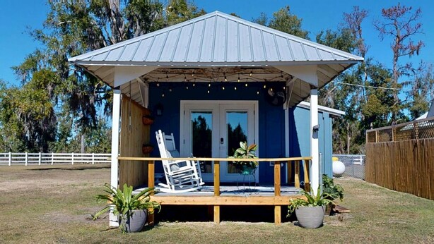 A small, single-story building with a porch, a white chair, and two potted plants. - The Nest ~ Near Music Park + Lake Views (Live Oak)