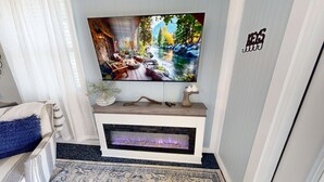 A living room with a flat-screen TV mounted above a fireplace, a decorative wall sign, and a patterned rug. - The Nest ~ Near Music Park + Lake Views (Live Oak)