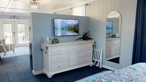 A bedroom with a large bed, a dresser with a mirror, and a TV on the wall. - The Nest ~ Near Music Park + Lake Views (Live Oak)