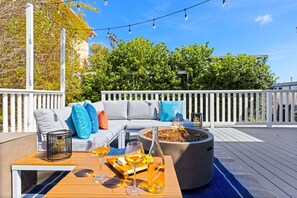 An outdoor deck with a sofa, a fire pit, and a table with drinks and a bottle. - Point Loma Cozy Retreat - Spa l AC l Parking (San Diego)