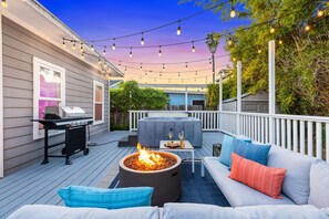Una terraza al aire libre con una parrilla, un hogar para fuego, un sofá y luces colgantes.