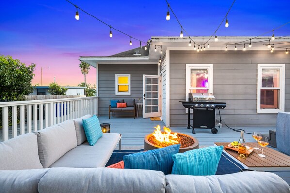 A deck with a fire pit, outdoor furniture, and string lights. - Point Loma Cozy Retreat - Spa l AC l Parking (San Diego)