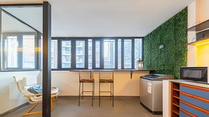 A compact kitchen with a green wall, a microwave, and a small dining area with chairs.