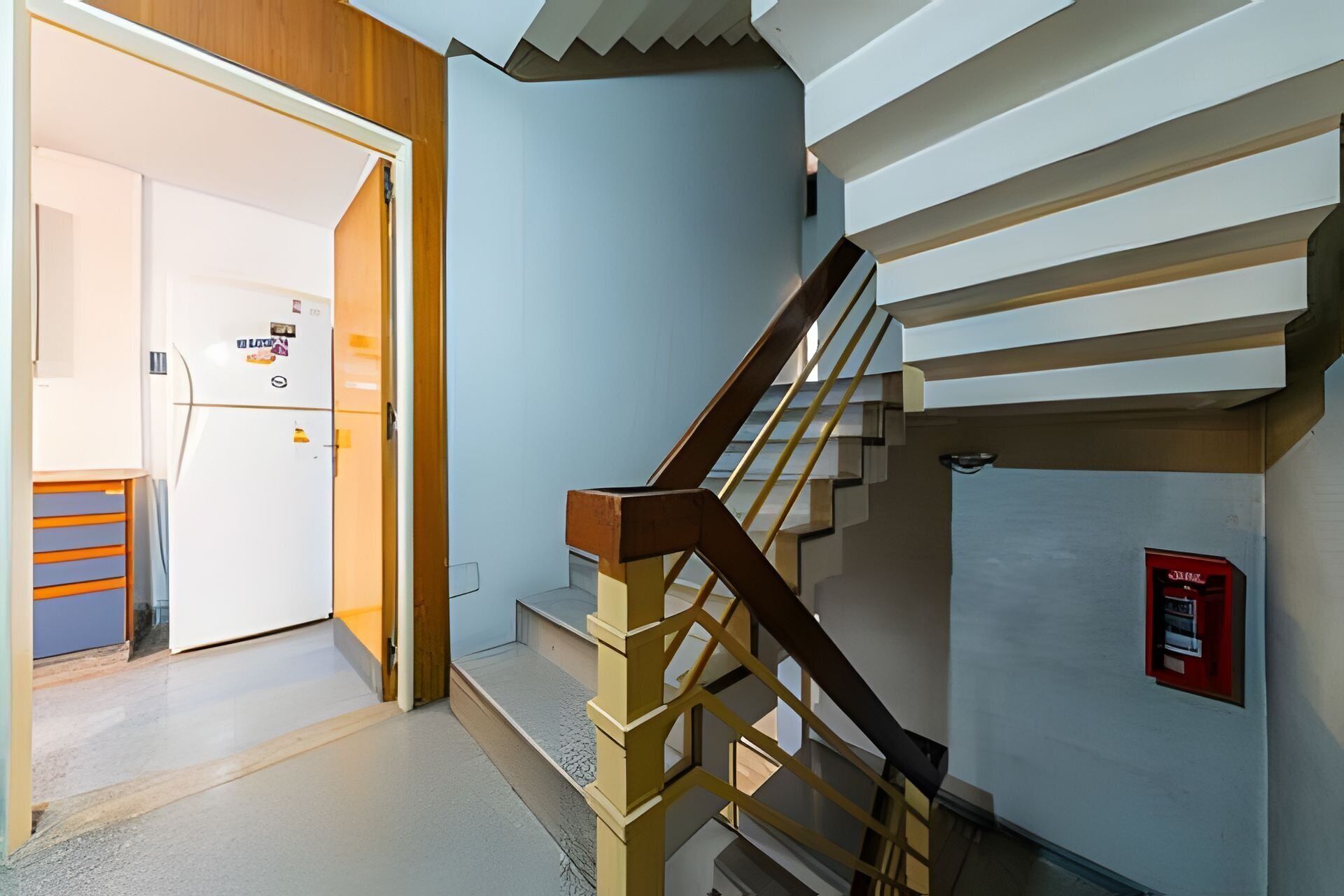 A modern interior with a staircase, a door leading to a room, and a fire alarm on the wall.