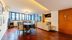 A modern living room with a dining table, chairs, a fireplace, and large windows.