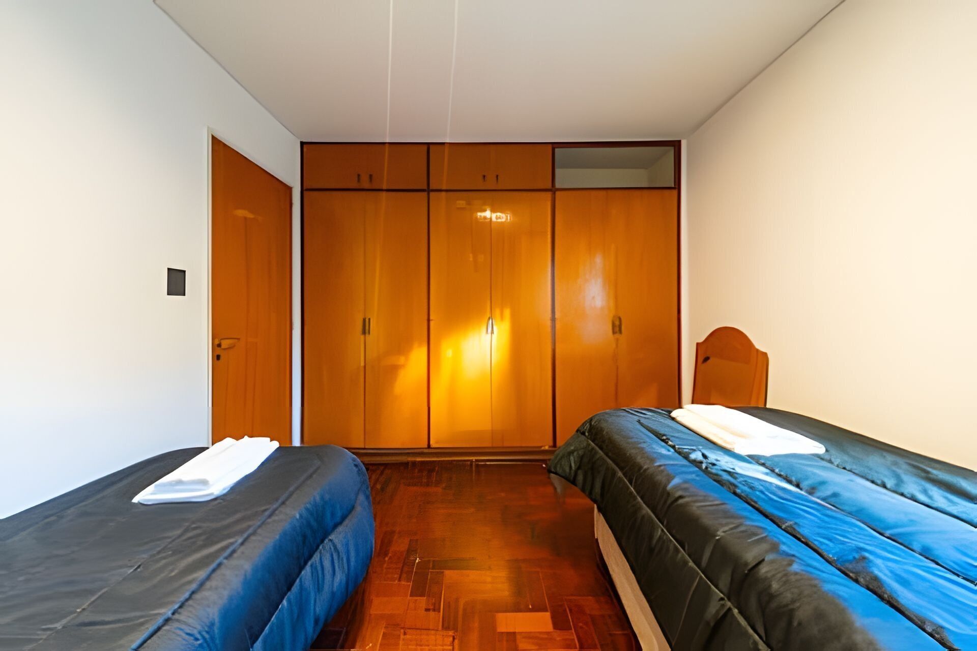 Una habitación con dos camas individuales, armarios de madera y una silla de madera pequeña.