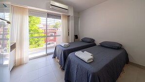 Habitación de hotel con dos camas, una ventana con cortinas, un equipo de aire acondicionado y vistas a edificios.