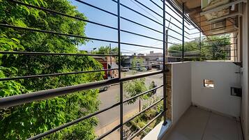 A balcony with metal railings overlooking a street with buildings and greenery.