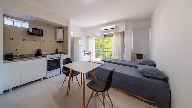Habitación compacta y moderna con kitchenette, una mesa de comedor con dos sillas y una cama con dos almohadas.