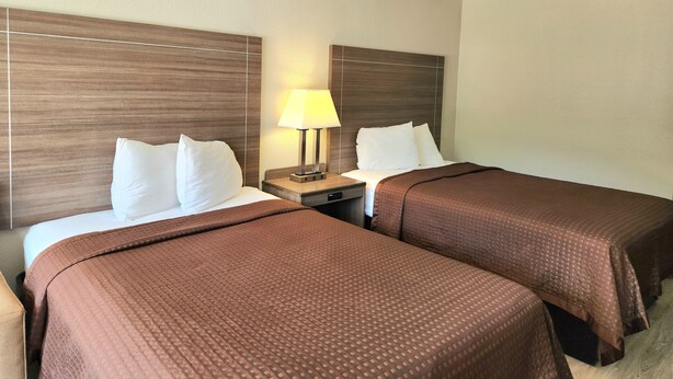 Une chambre d’hôtel avec deux lits, une table de chevet avec une lampe et une tête de lit en bois.