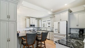 A modern kitchen with white cabinetry, a marble countertop, and two bar stools. - Bayberry House- 11BR/9BA in Ocean City NJ (Ocean City)