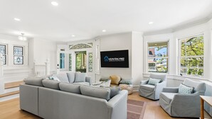 A modern living room with a grey sofa, two armchairs, a flat-screen TV, and large windows. - Bayberry House- 11BR/9BA in Ocean City NJ (Ocean City)