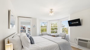 A modern hotel room with a bed, a desk, a chair, a TV, and large windows. - Bayberry House- 11BR/9BA in Ocean City NJ (Ocean City)