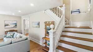 A spacious living room with a staircase, a sofa, and wall art. - Bayberry House- 11BR/9BA in Ocean City NJ (Ocean City)