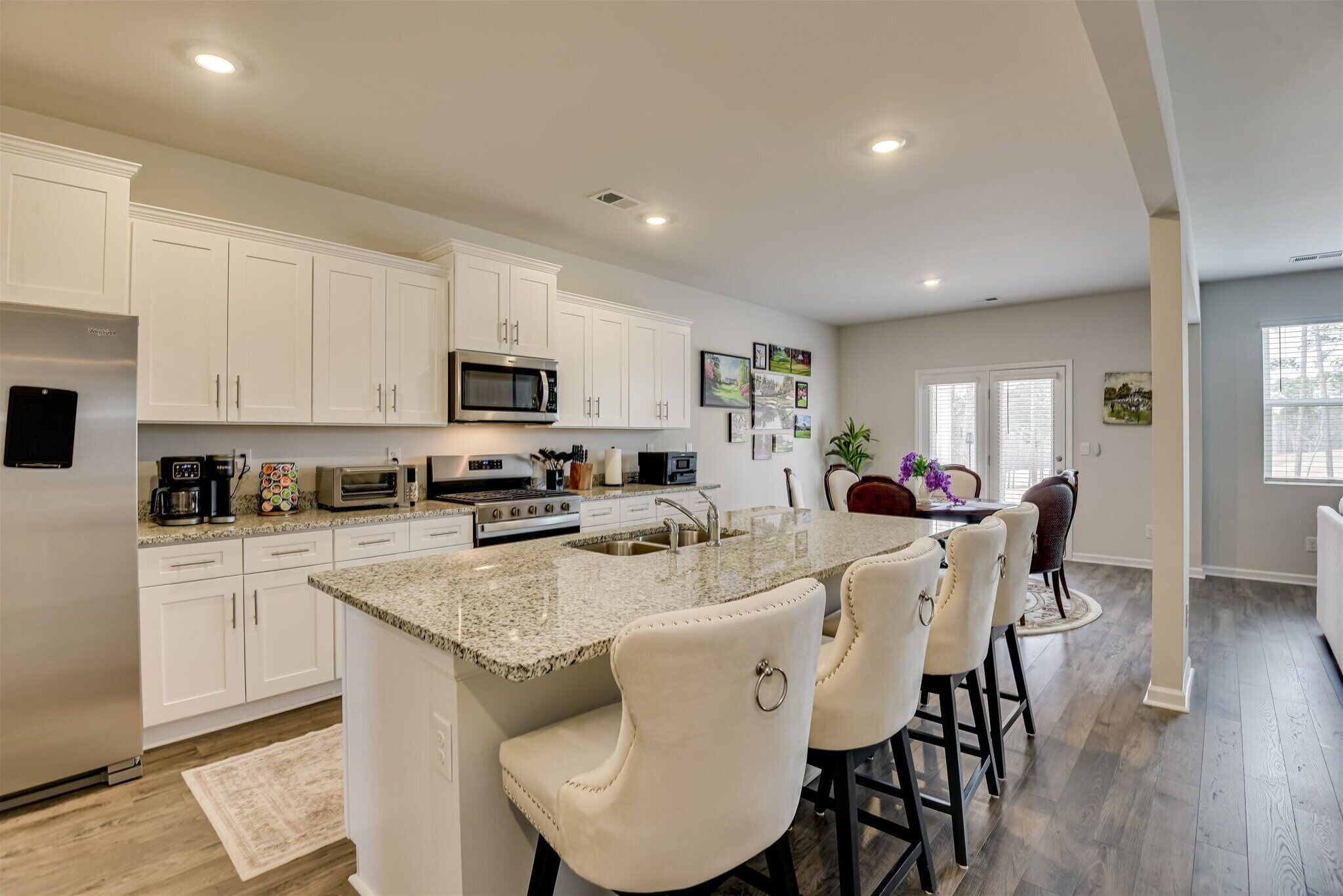 Una cocina moderna con gabinetes blancos, encimera de granito y una isla central con taburetes de bar.