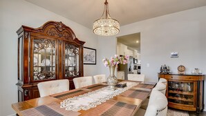 Comedor con una mesa de madera, sillas blancas tapizadas, un aparador decorativo y una araña.