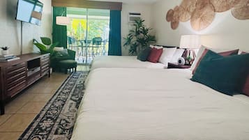 Una camera d'albergo con un letto, una scrivania, una sedia, una TV e un balcone con piante.