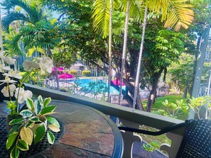 Un balcone con vista su una piscina, immerso nel verde e con piante in vaso.