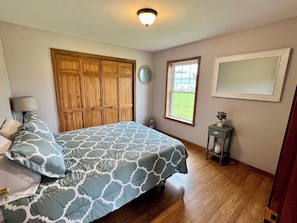 A bedroom with a bed, wooden wardrobe, window, and a small table with a lamp.