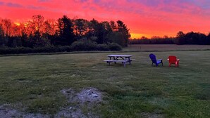 Piknikalue, jossa on pöytä ja tuoleja, vehreällä niityllä ja taustalla auringonlasku.