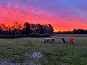 A picnic area with a table and chairs in a grassy field with a sunset in the background.