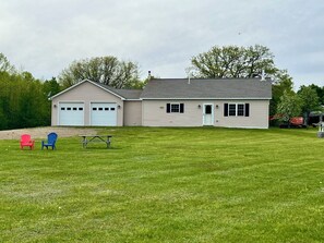 A two-story house with a garage, a front door, and a small lawn with two Adirondack chairs.
