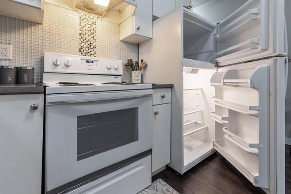Una cocina con estufa blanca, refrigerador abierto y salpicadero de azulejos.