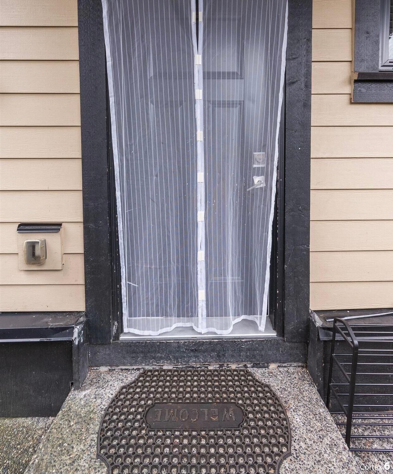A house entrance with a black door, a mesh screen, and a welcome mat.