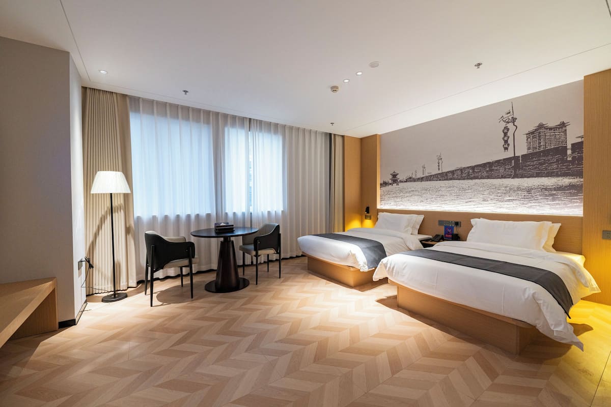 A hotel room with two beds, a desk, a chair, and a large window with curtains.