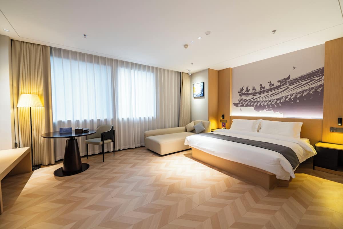 A modern hotel room with a large bed, a desk, a chair, and a sofa.