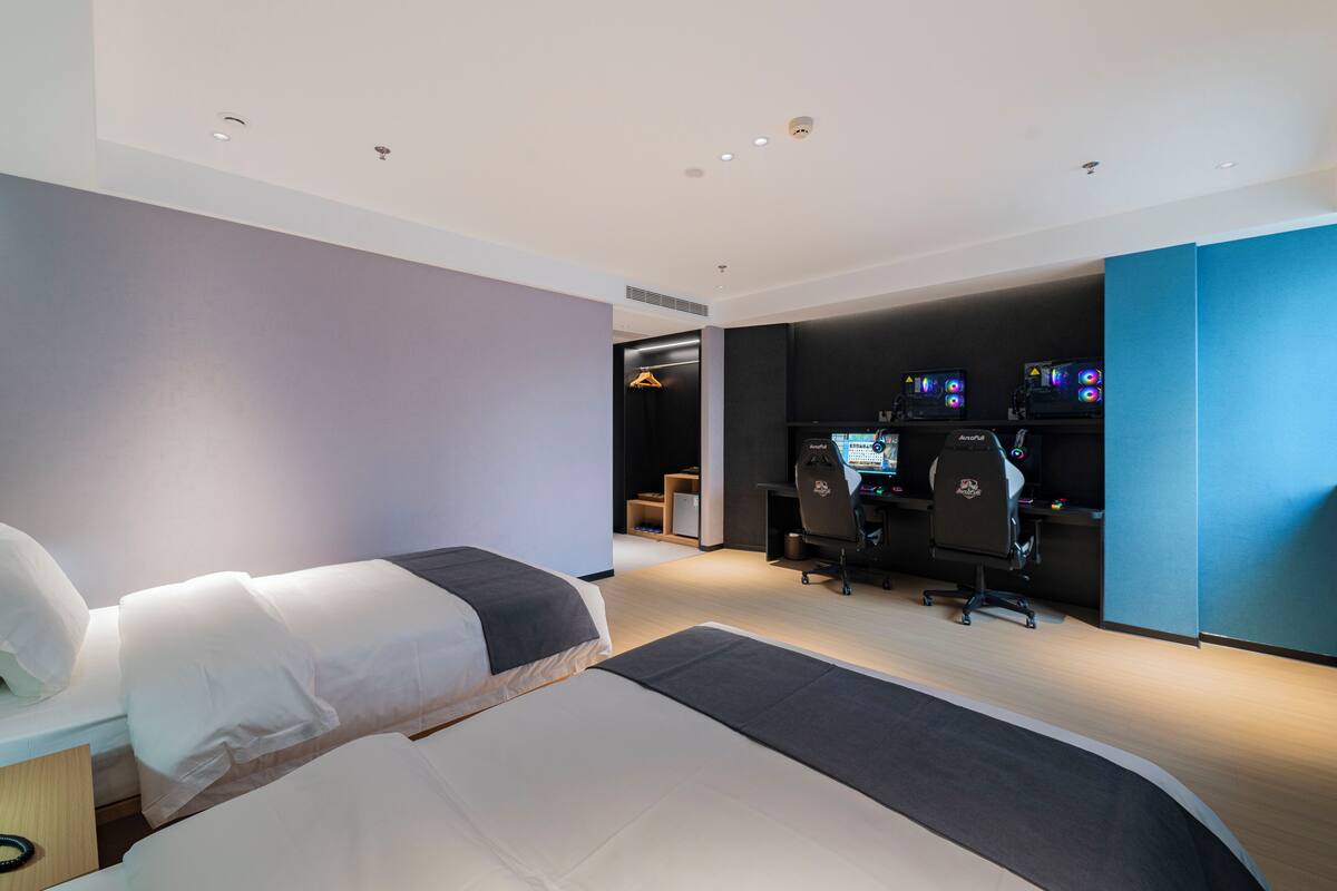 A modern hotel room with two beds, a desk with a computer, and a seating area with chairs.