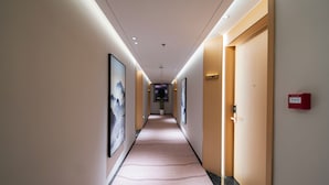 A hotel hallway with framed artwork on the walls, a carpeted floor, and a door with a number sign. - XINGHEHOTEL (Xi'an)