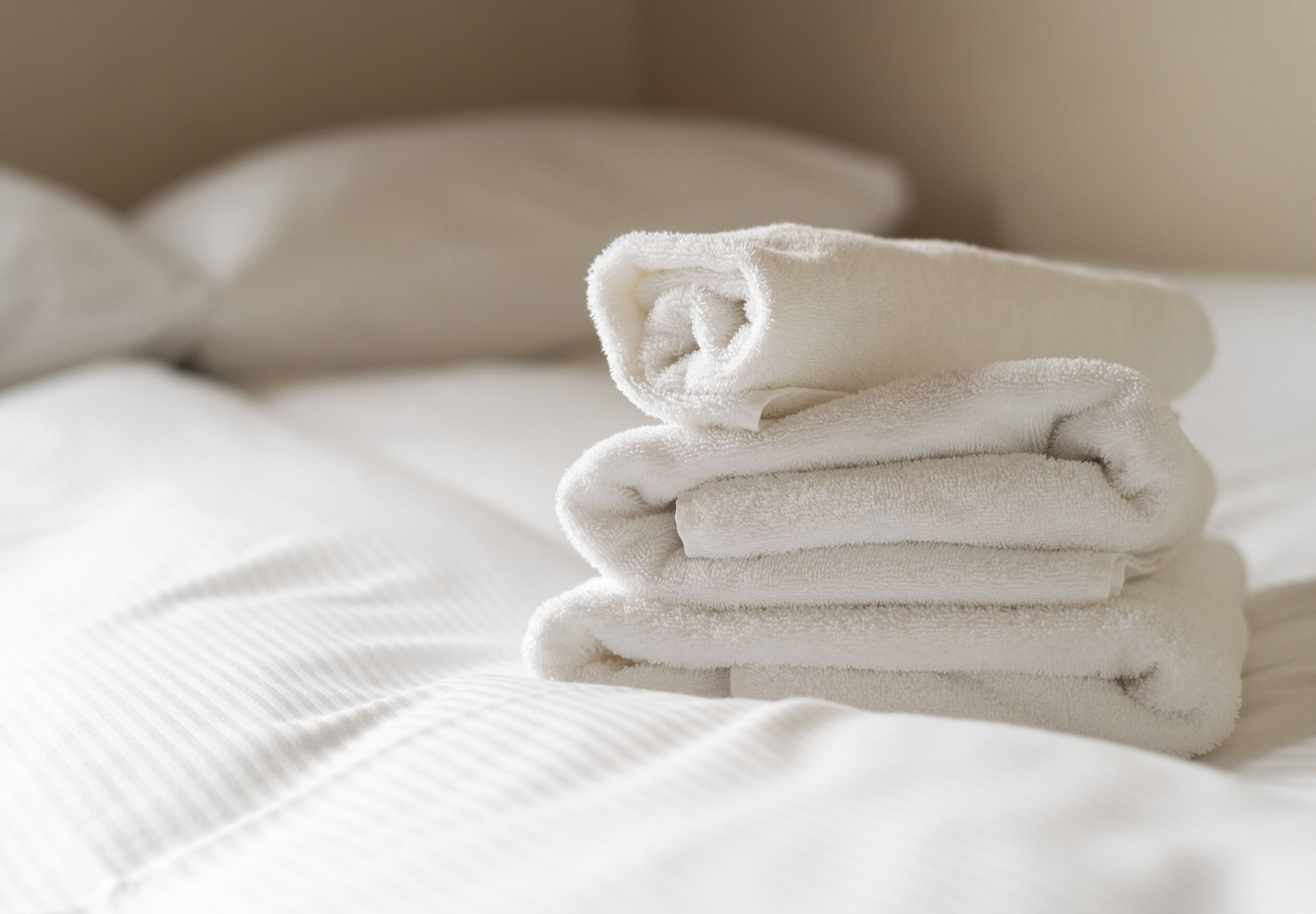 Un ordinato mucchio di asciugamani bianchi su un letto con un cuscino bianco.