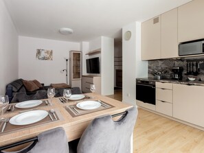 Cocina moderna con microondas, estufa y cafetera. Hay un comedor con una mesa lista para cuatro personas, y un sofá al fondo.