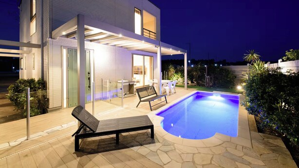 Une maison moderne dotée d’une piscine, d’un espace salon extérieur et d’un patio couvert.