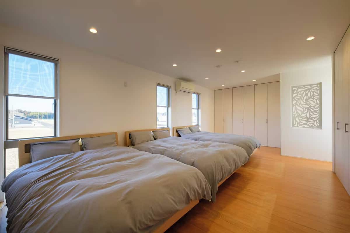 A modern bedroom with two beds, a large window, and a wardrobe.