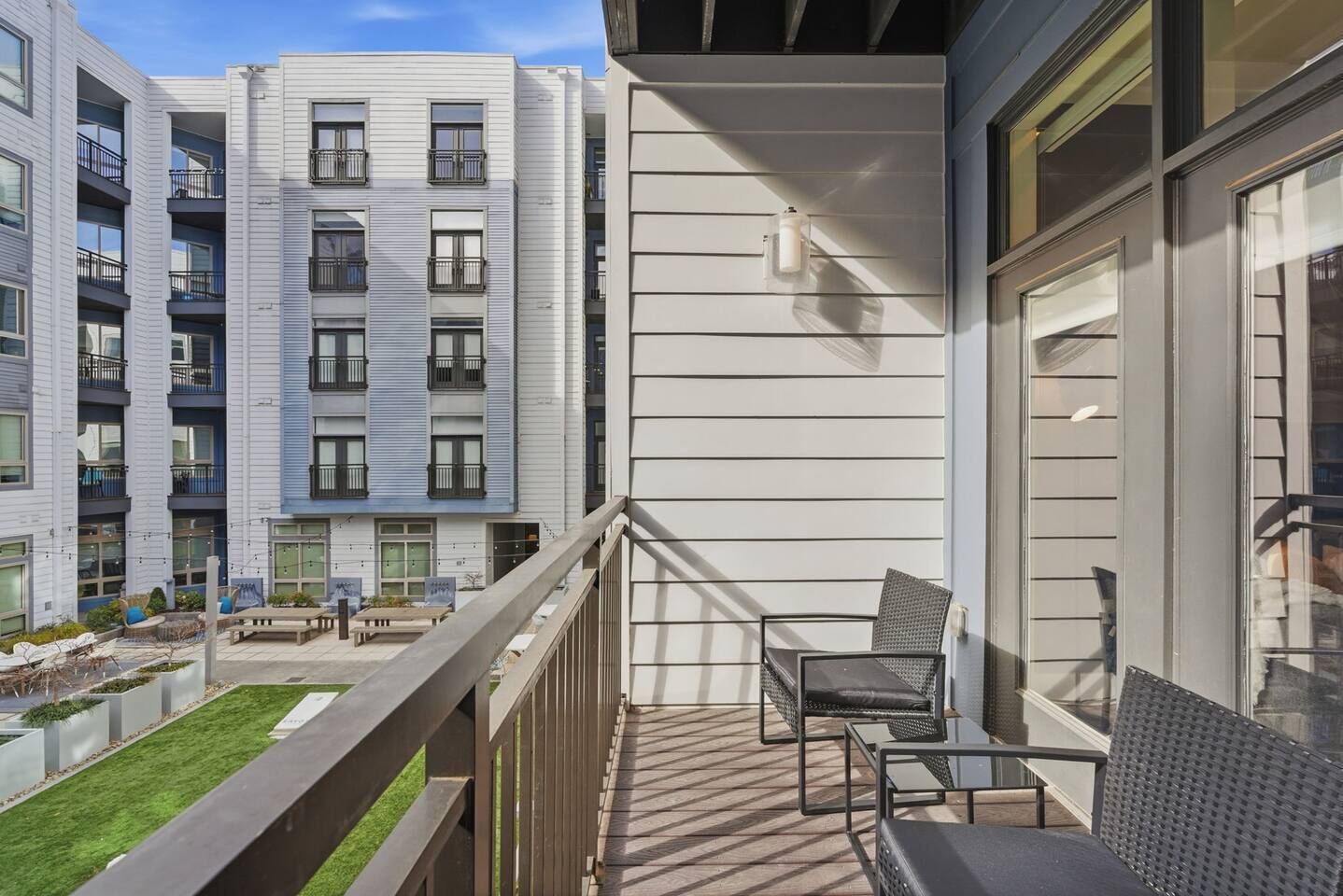Een balkon met buitenmeubilair, uitzicht op omliggende gebouwen en een kleine tuin.