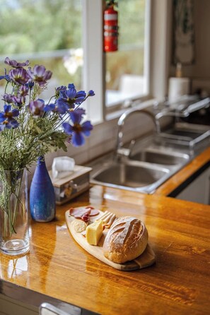 A kitchen counter with a loaf of bread, a small plate with cheese and crackers, and a vase with flowers. - Seednest Treehouse Spectacular Mountain View (Monbulk)
