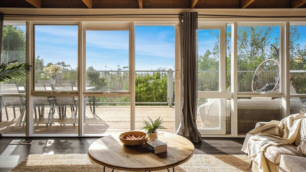 A spacious room with a large sliding glass door leading to an outdoor deck, a round wooden table, and a comfortable seating area. - Seednest Treehouse Spectacular Mountain View (Monbulk)